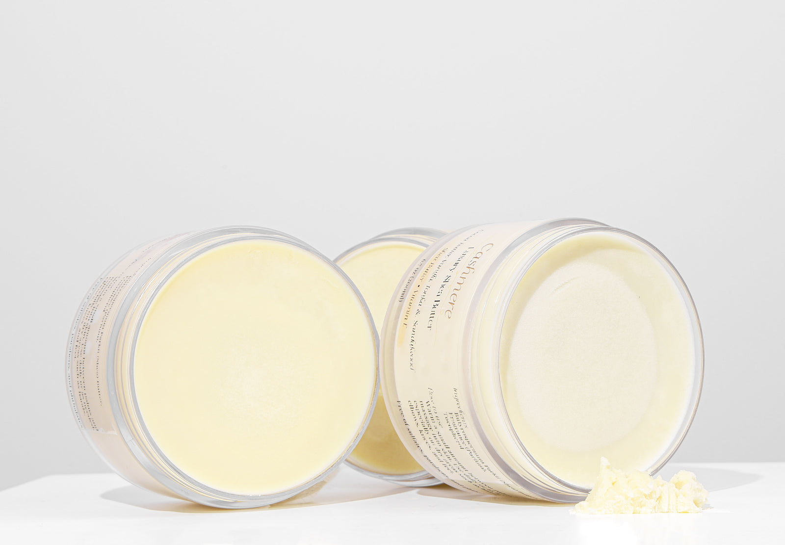 Three containers of a light-colored cream or balm on a white background